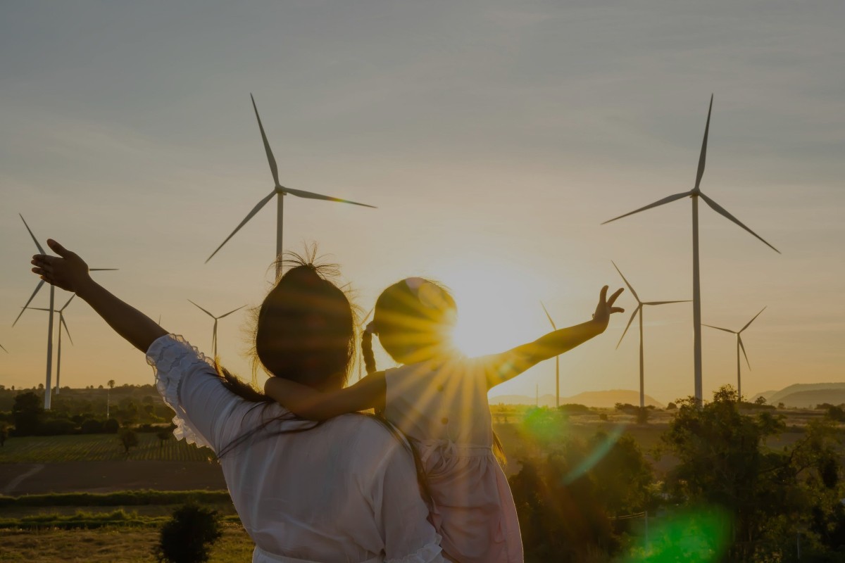 Parent and child in front of wind turbines at sunset.